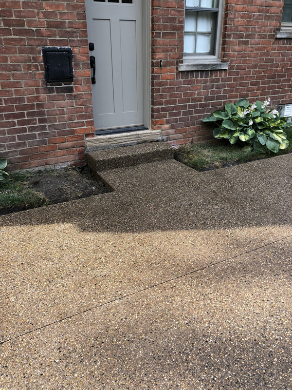 Residential driveway and front walkway featuring a custom exposed aggregate concrete finish leading to a brick home.