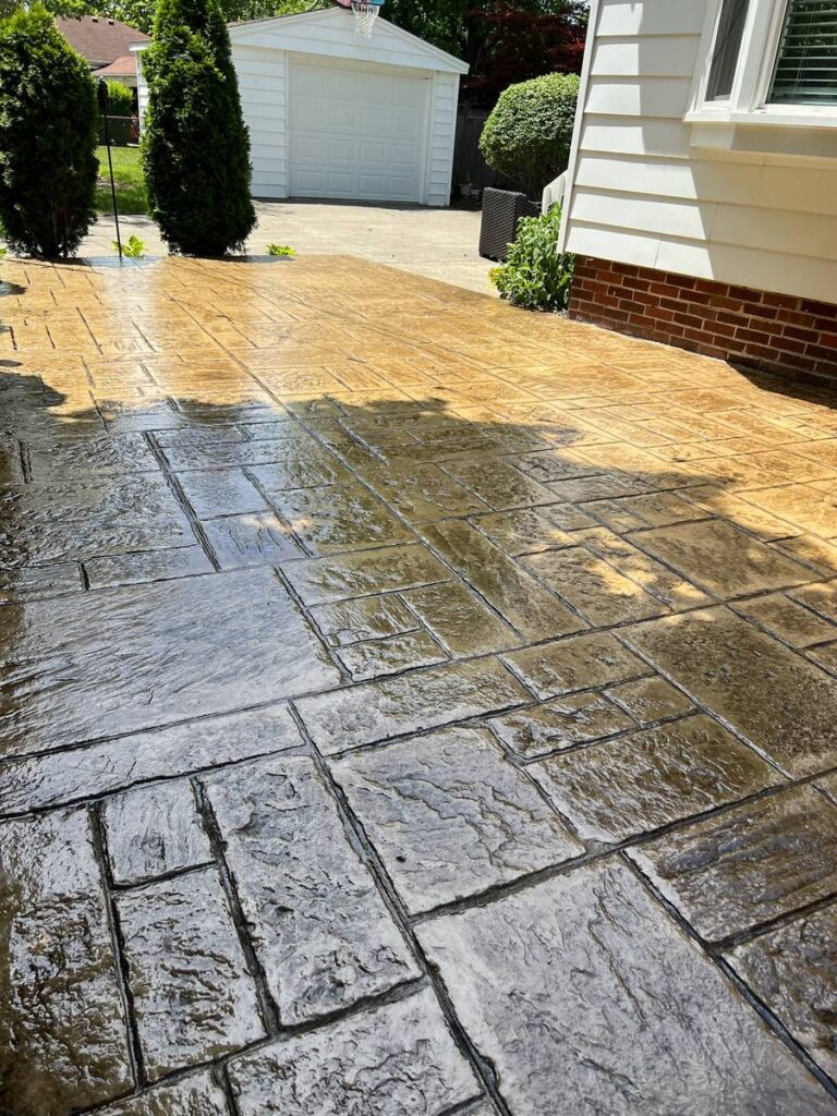 A newly sealed stamped concrete patio with an elegant ashlar slate pattern installed next to a residential brick home.