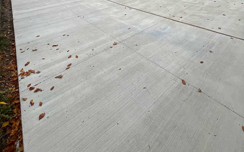 A freshly poured concrete driveway featuring a slip-resistant broom finish and clean control joints, completed by expert concrete contractors.