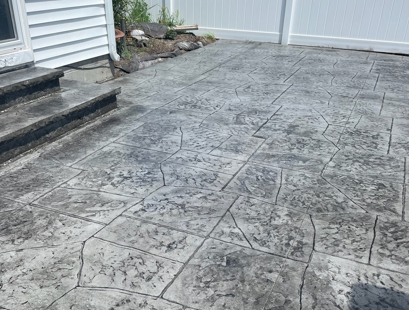 A beautiful grey stamped concrete patio with a random stone pattern and matching steps, installed by expert concrete contractors.