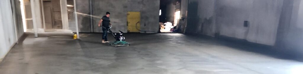 Professional concrete contractors using a walk-behind power trowel to smooth and finish a large commercial warehouse floor.