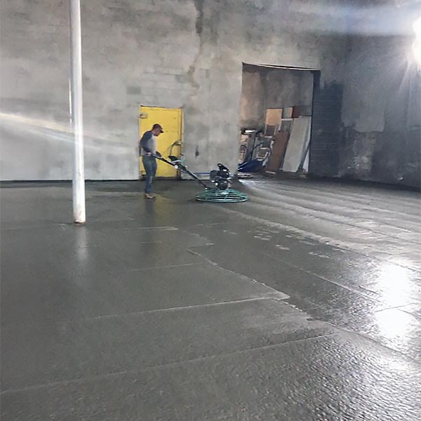 Contractor using a power trowel to finish and smooth newly poured concrete floors in a commercial space.