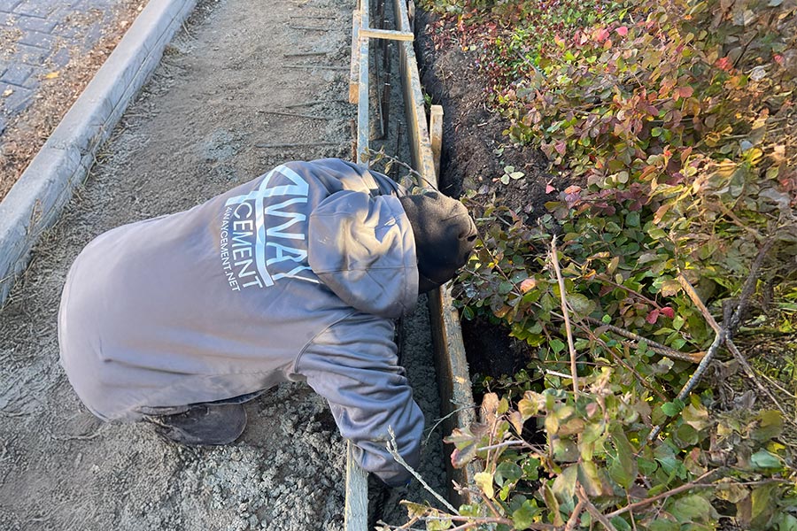 A worker in a 4 Way Cement hoodie setting up wooden forms and rebar for a curb installation, representing local concrete contractors.