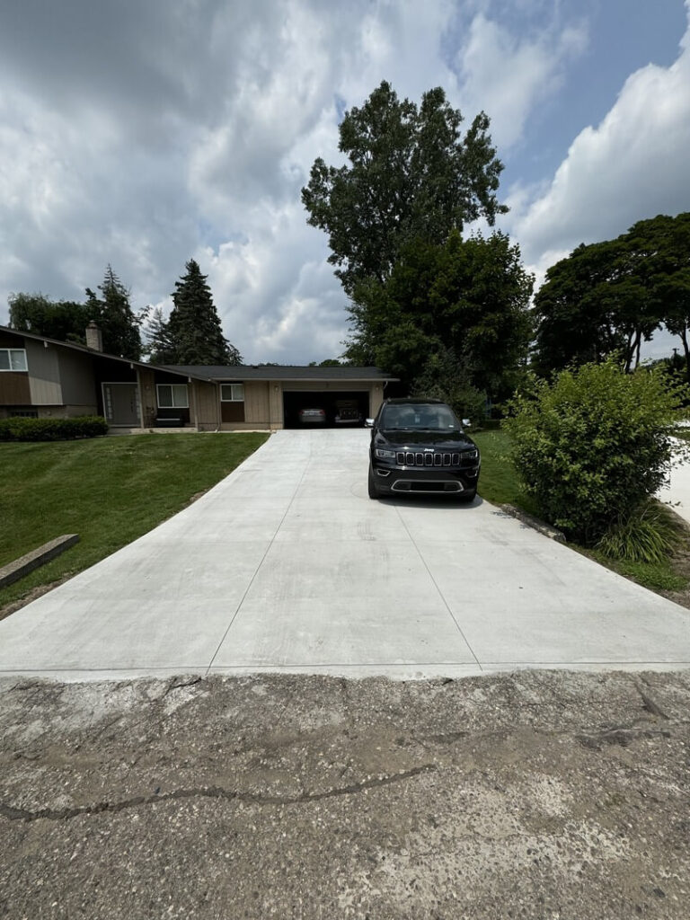 Newly installed regular concrete driveway leading to a residential home with a parked vehicle.